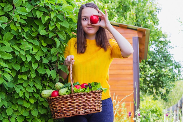 Foto una joven sostiene una canasta con un cultivo contra el fondo de un jardín.