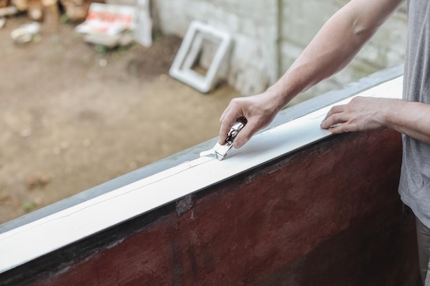 Un joven sostiene un cuchillo de construcción en sus manos y limpia plástico de silicona