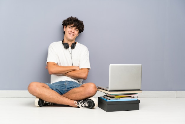 Joven con su computadora portátil sentado uno el piso riendo