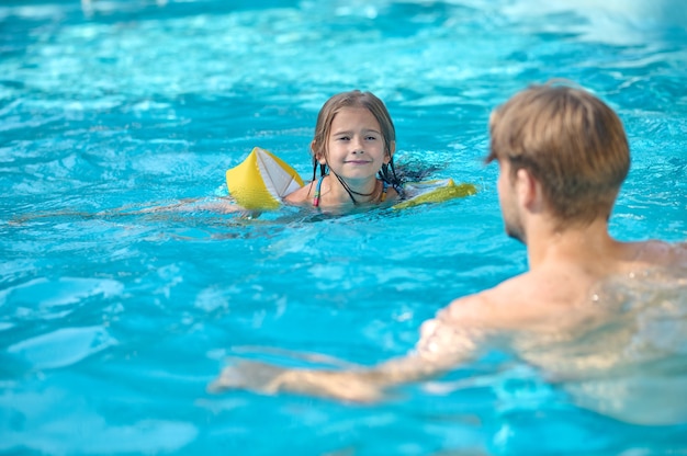 Un joven y su hija nadando en la piscina y mirando disfrutados