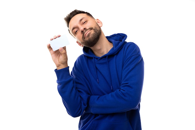 Un joven con una sudadera azul de fondo blanco tiene una tarjeta bancaria en las manos