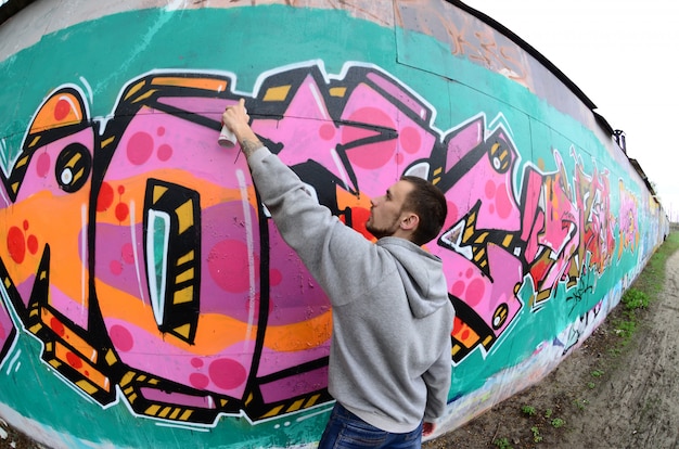 Un joven con una sudadera gris pinta graffiti.