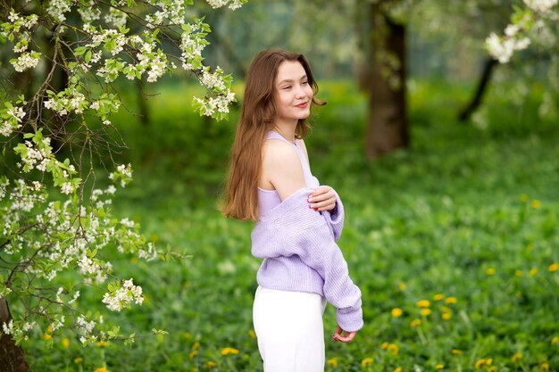 Una joven con un suéter junto a flores blancas en un árbol.