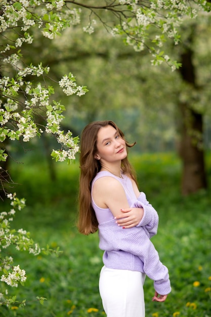 Una joven con un suéter junto a flores blancas en un árbol.