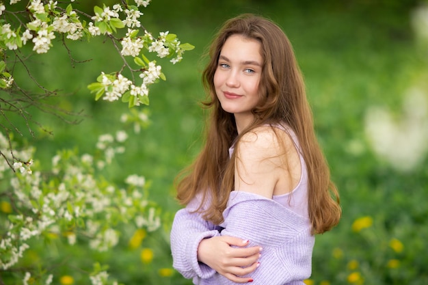 Una joven con un suéter junto a flores blancas en un árbol.