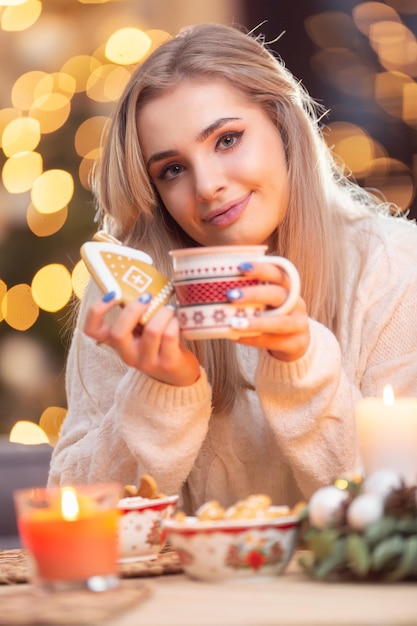 Una joven con un suéter de lana sosteniendo un pan de jengibre y una taza con té, café o ponche de Navidad