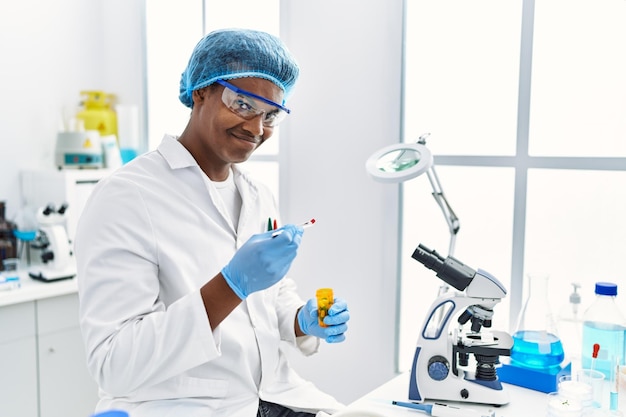 Joven del sureste con uniforme de científico sosteniendo una píldora en el laboratorio