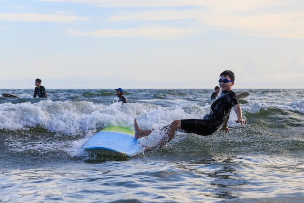 Joven surfista asiático cayendo de la tabla a la ola del mar con cara feliz y divertida