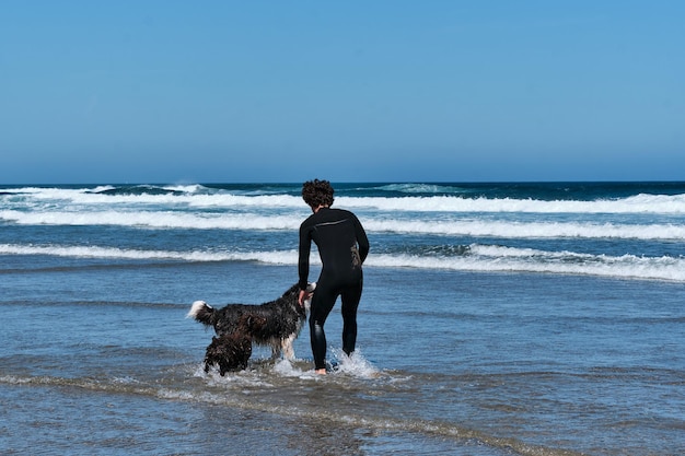 Joven surfista jugando con su perro border collie junto al mar