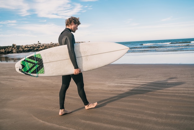 Joven surfista de pie en el océano con su tabla de surf en un traje de surf negro. Concepto de deporte y deporte acuático.