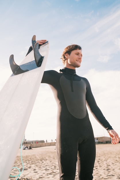 Joven surfista de pie en el océano con su tabla de surf en un traje de surf negro