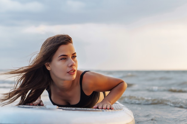 Joven surfista sexy mujer acostada sobre su sup junta mirando a la puesta del sol.