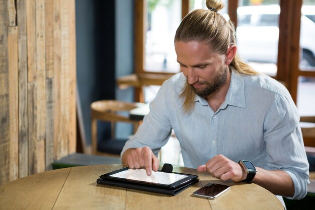 Joven con tableta digital en la mesa de madera en el café