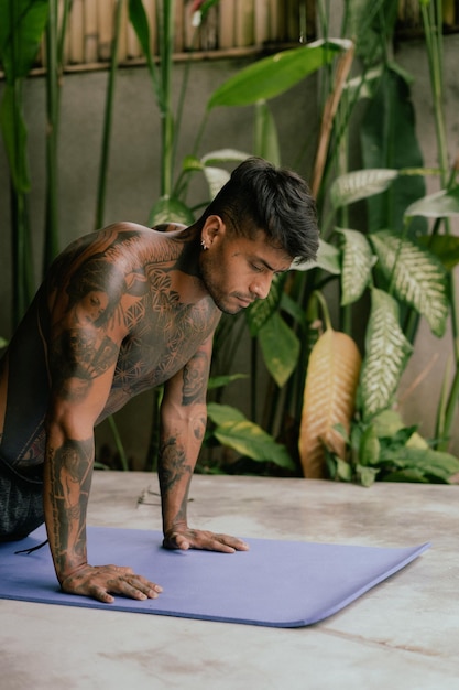 Joven tatuado latinoamericano practica yoga al aire libre durante las vacaciones de retiro en Bali, estiramiento, meditación, bienestar