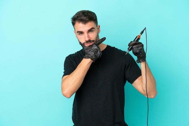 Joven tatuador hombre aislado sobre fondo azul pensando