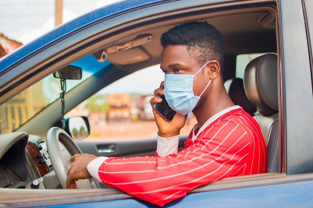 Joven taxista africano guapo con máscara facial que previene, previene, se previene del brote en la sociedad y llama con su teléfono móvil