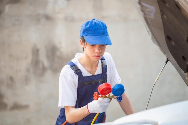 Joven técnico revisa la recarga de refrigerante del sistema de aire acondicionado del automóvil Reparador que sostiene la herramienta del monitor para verificar y reparar el sistema de aire acondicionado del automóvil