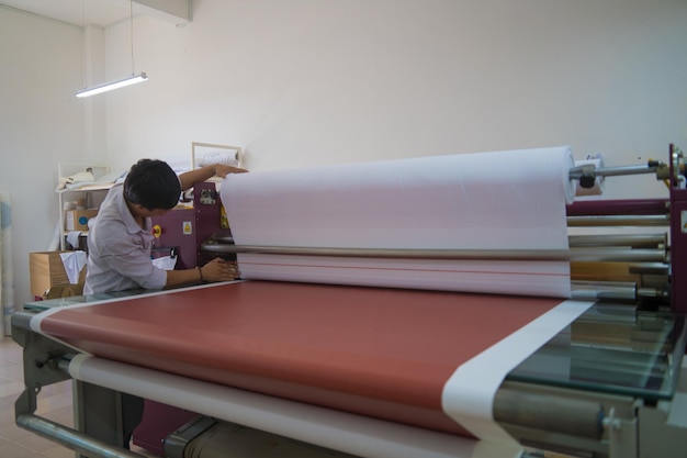 Un joven técnico trabajador asiático hace un objeto en una máquina de prensa de calor por sublimación en una impresora digital