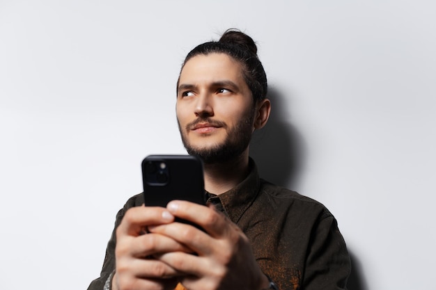 Joven con teléfono inteligente en las manos mirando hacia otro lado sobre fondo blanco.