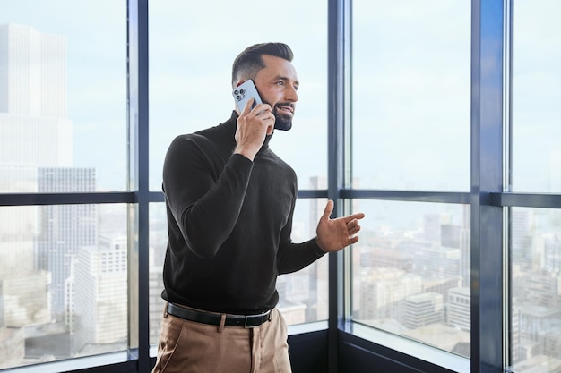 Joven con un teléfono inteligente parado cerca de la ventana