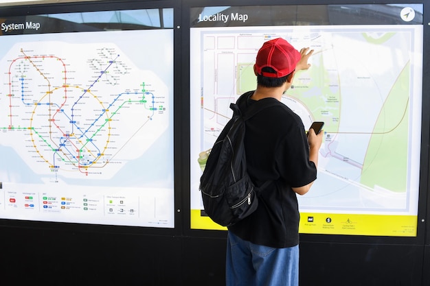Joven con teléfono inteligente señalando el mapa del metro en la estación