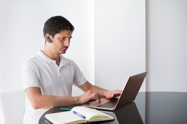 Joven teletrabajando desde su casa en su computadora portátil y usando un auricular.