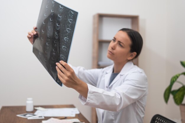 Foto una joven terapeuta examina las imágenes de resonancia magnética del paciente sentada en la oficina de la clínica