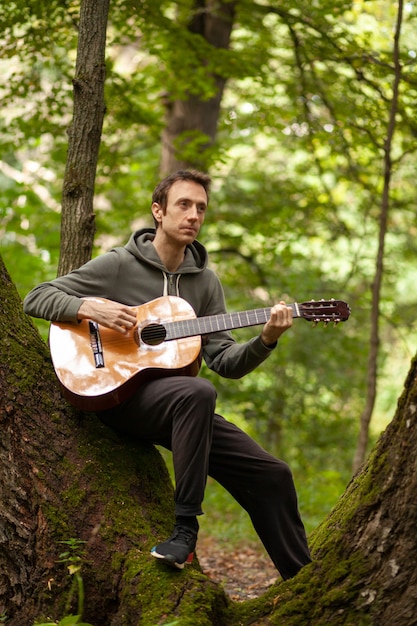 Joven toca la guitarra acústica en la naturaleza en el bosque