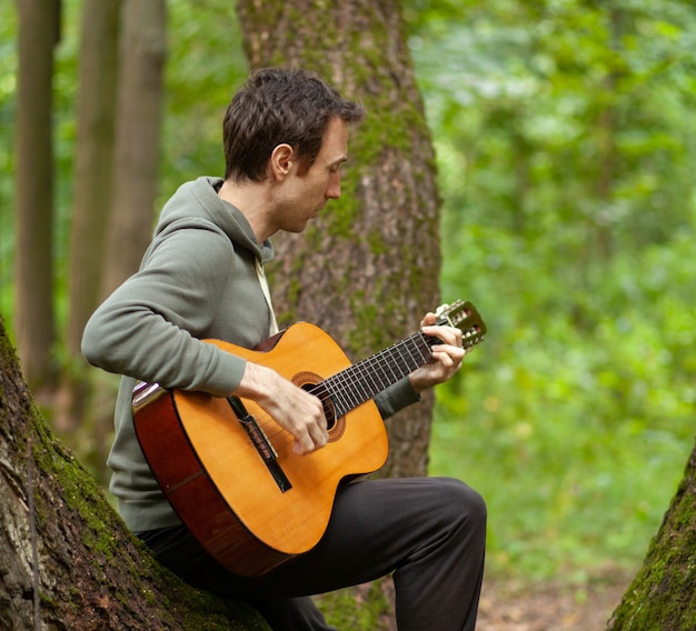 Joven toca la guitarra acústica en la naturaleza en el bosque