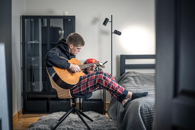 Un joven toca la guitarra acústica en su habitación en casa.