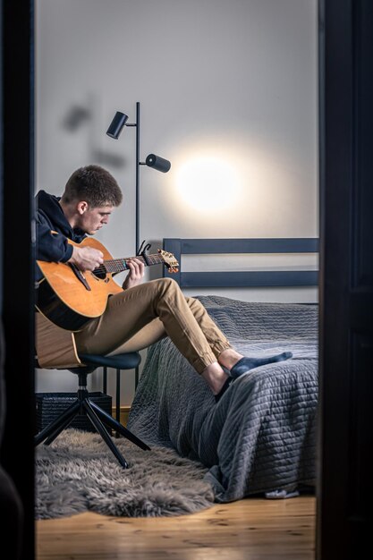 Un joven toca la guitarra acústica en su habitación en casa.