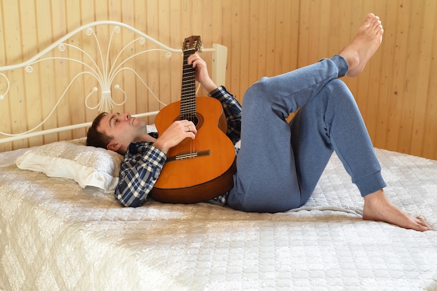 Joven tocando la guitarra y acostado en una cama