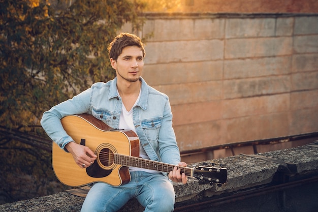 Joven tocando la guitarra en la ciudad sobre fondo de rayos de sol