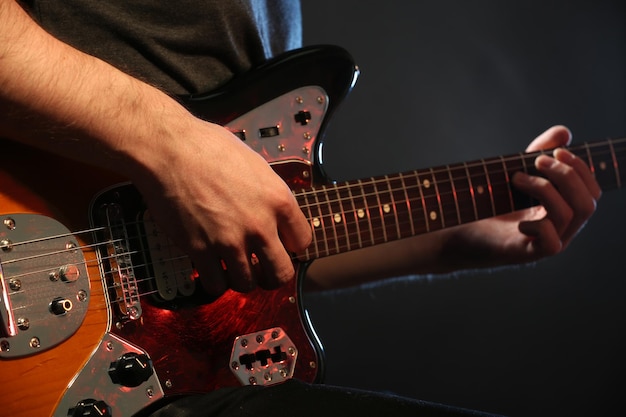 Joven tocando la guitarra eléctrica sobre fondo oscuro