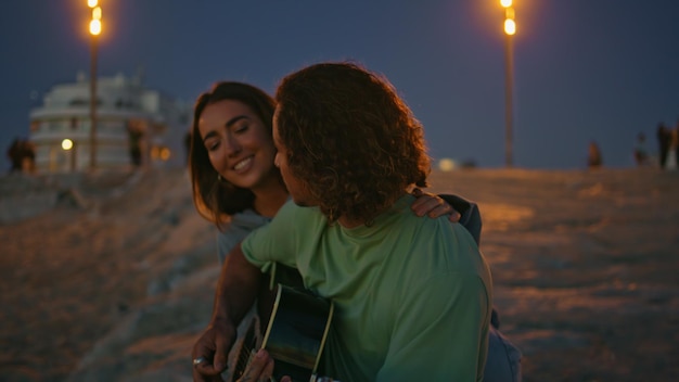 Joven tocando la guitarra por la noche playa de cerca adolescentes noche romántica