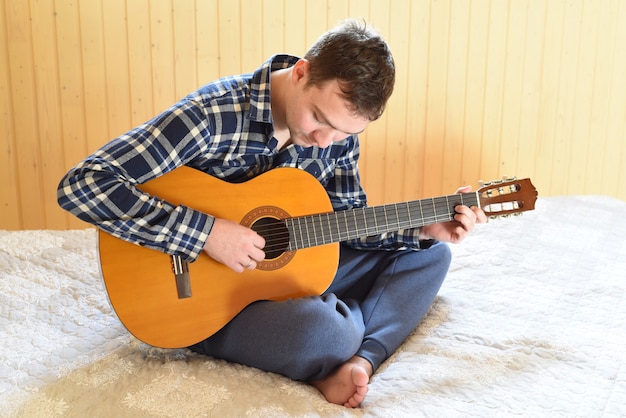 Joven tocando la guitarra y sentado en una cama