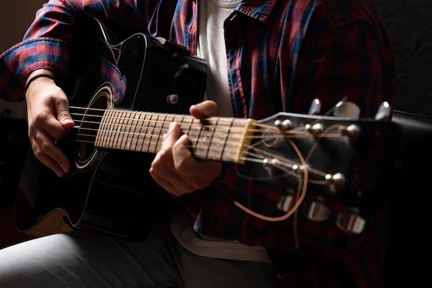 Joven tocando la guitarra vista de cerca fondo oscuro