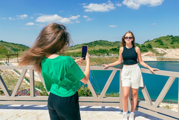 Una joven toma una foto de su amiga frente al lago con un teléfono móvil El concepto de personas influyentes en los viajes Montaña en el fondo