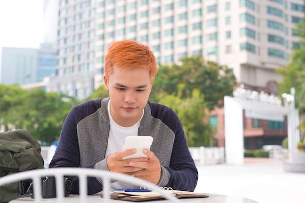 Joven tomando café en la cafetería y mirando la pantalla del teléfono