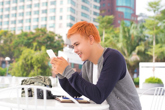 Joven tomando café en la cafetería y mirando la pantalla del teléfono