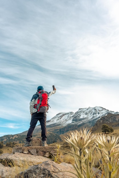 Joven tomando un selfie con un teléfono móvil inteligente haciendo senderismo en las montañas