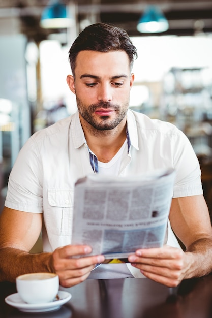 Foto joven tomando una taza de café leyendo periódico