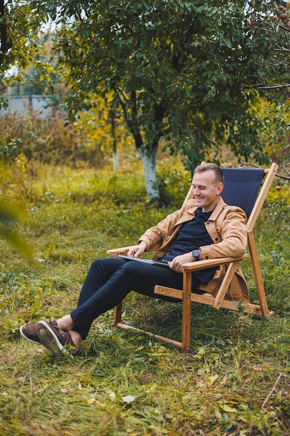 Un joven trabaja en una computadora portátil al aire libre Un joven autónomo descansa en el bosque Trabajo remoto recreación activa en el verano Concepto de personas de turismo hombre sentado en una silla al aire libre