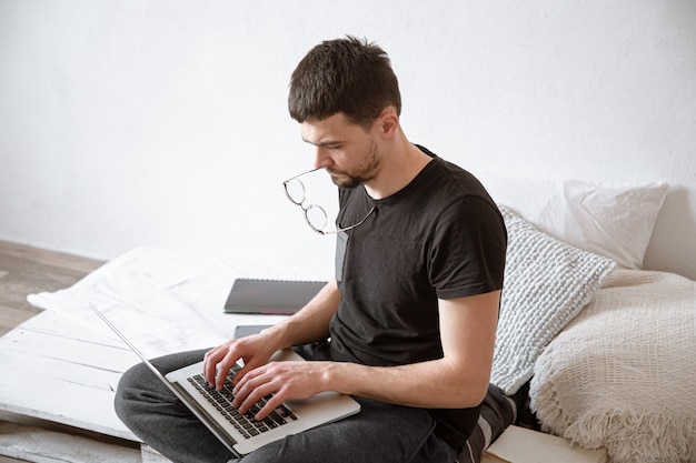 Un joven trabaja de forma remota detrás de una computadora portátil en casa. Freelance y concepto de Internet.