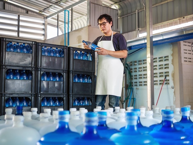 Joven trabajador asiático que usa gafas trabajando en el control de agua potable embotellada