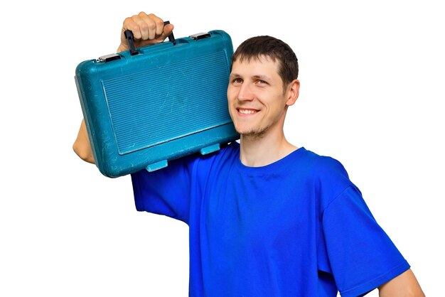 Un joven trabajador con una camiseta azul sostiene una maleta con herramientas en el hombro y sonríe Reparaciones urgentes de guardia