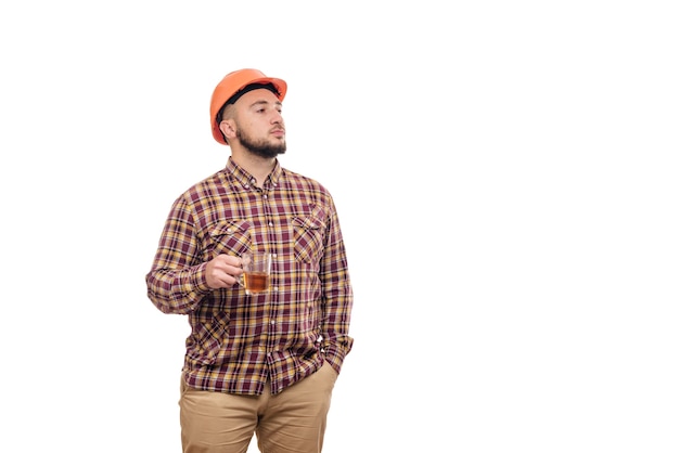 Joven trabajador en un casco naranja sostiene una taza de té, fondo blanco aislado