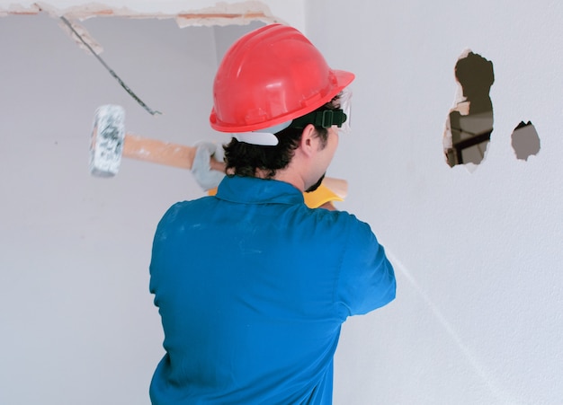 Foto joven trabajador con un casco de protección rojo y vistiendo un traje de caldera azul. concepto de demolición