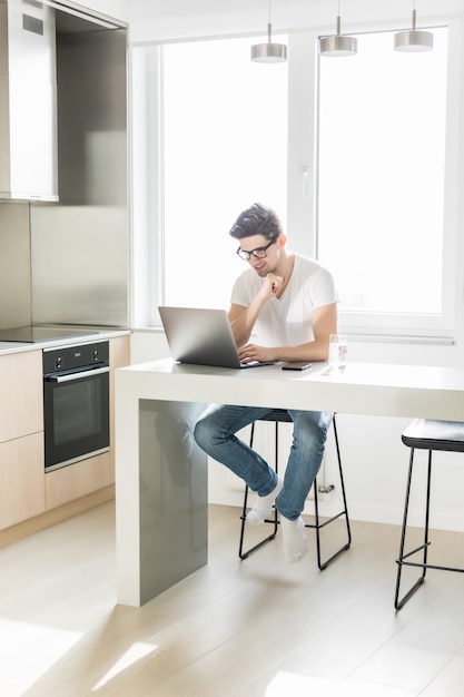 Joven trabajador en la cocina usando laptop sonriendo