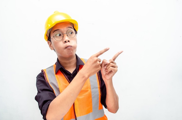 joven trabajador de la construcción asiático sonriendo y señalando con el dedo con expresión feliz y conmocionada.